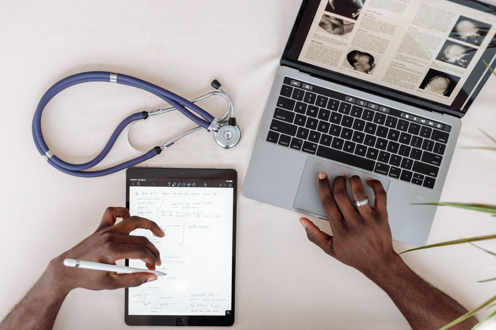 A tablet and laptop on a white desk with a stethoscope